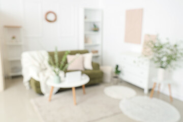 Stylish room with green sofa, coffee table and blooming branches, blurred view