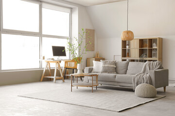 Interior of stylish living room with sofa, coffee table, workplace and blooming tree branches in vase