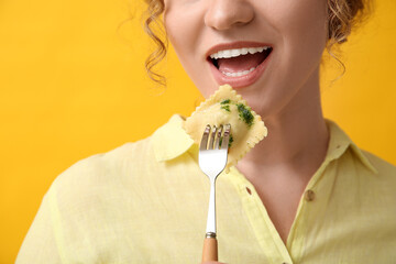 Beautiful young woman holding fork with tasty ravioli on yellow background