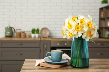Cup of coffee and vase with yellow flowers on table in stylish kitchen