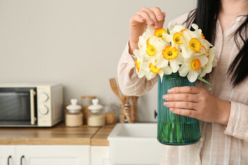 Young woman holding vase with yellow flowers on table in stylish kitchen