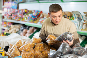 Man is in department of market with packaged products, holding plastic bag with raisins in his...