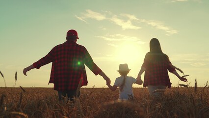 Father mother daughter running into wheat field holding hands. Happy family farmers run wheat...