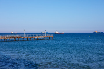 Pier in the sea with ships in the distance on the horizon. Blue sky over blue sea 