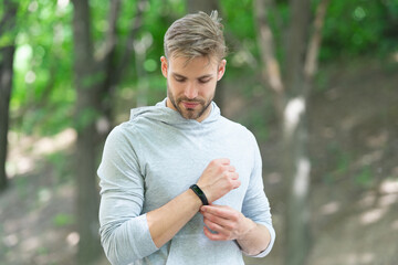 Sporty fit man with sport equipment checks time on smartwatch. Man tracking fitness results dressed in sportswear outdoor. Man runner with fitness gadget. Smartwatch for fitness