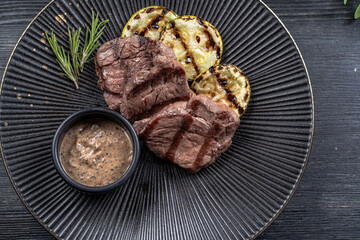 Fresh juicy delicious beef steak on a dark background. Meat dish with spices and herbs