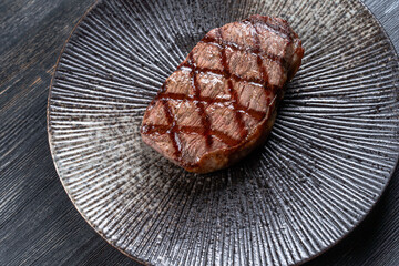 Fresh juicy delicious beef steak on a dark background. Meat dish with spices and herbs