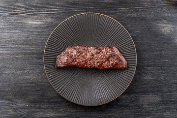 Fresh juicy delicious beef steak on a dark background. Meat dish with spices and herbs