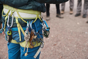 Unrecognizable person wearing a mountaineering harness from which climbing equipment is hanging: carabiners, slings, lanyards, ropes.