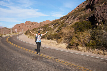 Obraz premium Woman hiker opening her arms in the middle of the road, carefree, happy, living an adventure during her vacations in the mountains of Potrerillos, Mendoza, Argentina.