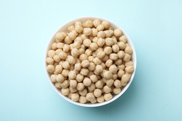 Tasty cereal balls in bowl on light blue table, top view