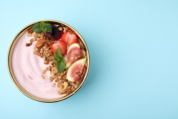 Bowl with yogurt, fruits and granola on light blue background, top view. Space for text