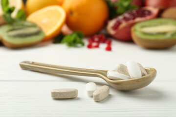 Different vitamin pills in spoon and fresh fruits on white wooden table