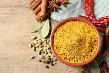Curry powder in bowl and other spices on wooden table, flat lay. Space for text