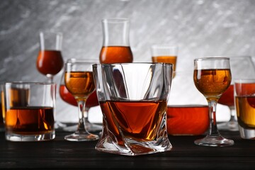 Different delicious liqueurs in glasses on dark wooden table