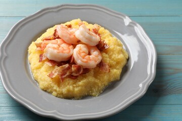 Plate with fresh tasty shrimps, bacon and grits on light blue wooden table, closeup