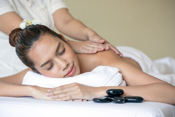 At the spa, young Asian woman receives soothing hot stone massage, with emphasis on wellness and...