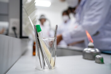A group of people are in a lab, with a glass beaker on a table