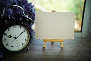 Empty card space for text message with wooden easel and alarm clcok on wooden background