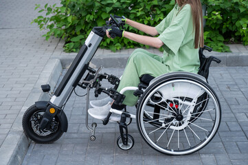 A faceless woman in a wheelchair with an assistive device for manual control. Electric handbike. 