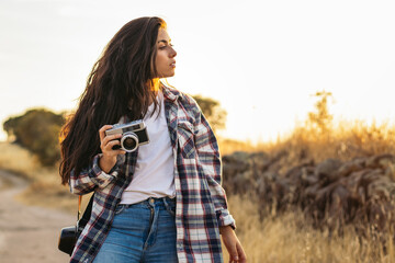 Young woman taking photos with analog camera in the field at sunset