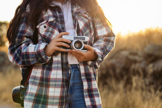 Unrecognizable woman taking photos with analog camera at sunset