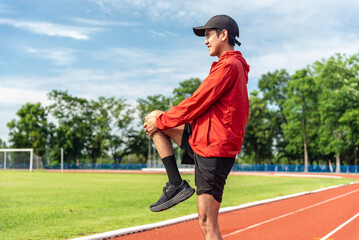 Young Asian man stretching his leg warm up before workout outdoor running track background. The man...