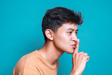 Side view of young Asian man keeps finger on lips, asks not tell secret information or keep silence
