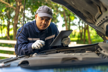 Asian automobile mechanic repairman wearing uniform and protection glove repairing a car engine...