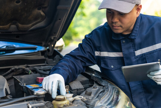 Asian automobile mechanic repairman wearing uniform and protection glove repairing a car engine automotive workshop with tablet, car service and maintenance, Repair service.