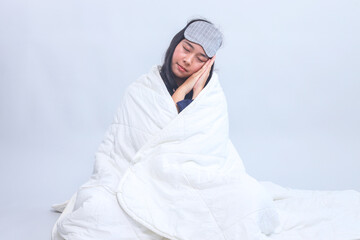 Full body of woman sitting in pajamas and sleep eye mask sleeping while covered with blanket