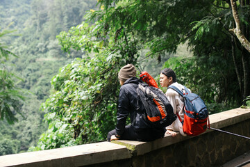 Back view of young man and woman sitting on the bench looking at beautiful nature view