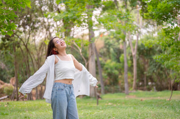 Naklejka premium A carefree Asian woman stands with her arms outstretched, embracing the serenity of nature in a park