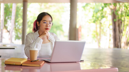 A focused female student working on her laptop while sitting at a table in her college cafeteria.