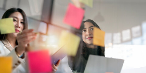 Business woman meeting at office and use post it notes to share idea. Brainstorming concept. Sticky note on glass wall.