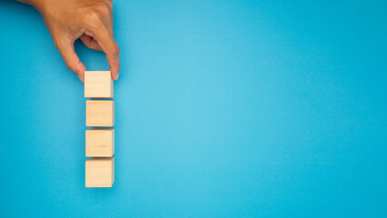 A hand is arranging wooden blocks in a vertical line on a vibrant blue background.