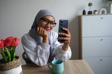 Beautiful Asian woman wear headscarves and glasses doing video call using smartphone at home