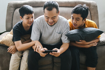 Two Young Boys Looking at Father Playing Mobile Games on Smartphone. Family Bonding, Spending Time...