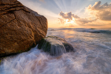 Long exposure photo of waves and rocks at sunrise.