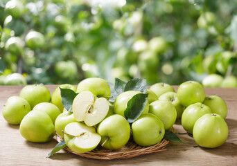 Green apples with leaves on wooden table on orchard garden background