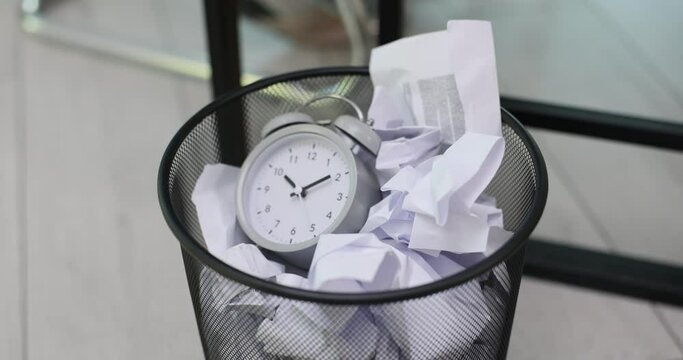 Alarm clock is thrown into a trash can made of crumpled paper