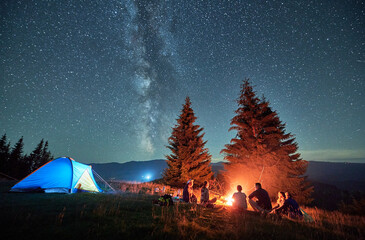 Night camping in mountains under starry sky. Group of people tourists having a rest near campsite,...