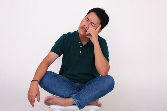 A man sitting on a stool is closing his eyes, while hand supporting his head