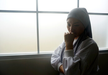 Young woman wear headscarves standing against window with sad expression 