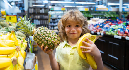 Happy little kid with fruits and vegetables at grocery store. Healthy food for young family with kids. Happy child with shopping cart full of fresh vegetables. Kids at grocery store or supermarket.