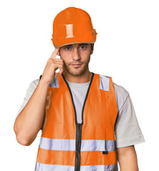 Young Hispanic worker in safety gear pointing temple with finger, thinking, focused on a task.