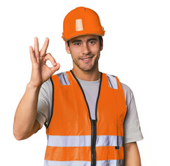 Young Hispanic worker in safety gear cheerful and confident showing ok gesture.