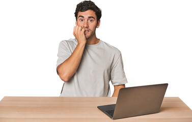 Hispanic young man working on laptop biting fingernails, nervous and very anxious.