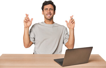 Hispanic young man working on laptop crossing fingers for having luck