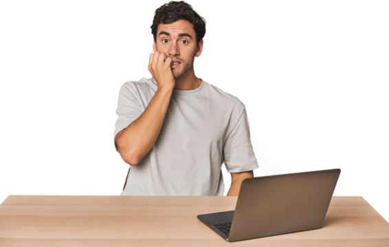 Hispanic young man working on laptop biting fingernails, nervous and very anxious.